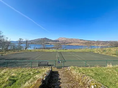 a tennis court with a bench next to a tennis court at Grace's Cottage in Port of Menteith