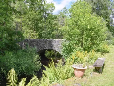 an old stone bridge with a bench in a park at Grace's Cottage in Port of Menteith
