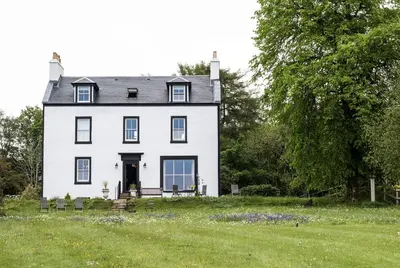 a white house with a grass field and trees at Pennygate Lodge in Craignure