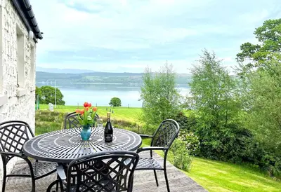 a table with a bottle of wine and flowers on a patio at Rowan Cottage in Blairmore