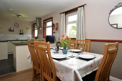 a dining room with a table with chairs and a kitchen at Rowan Cottage in Blairmore