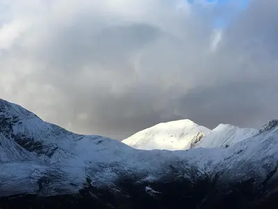 a group of snow covered mountains under a cloudy sky at Woodland Cabins, Glencoe in Ballachulish