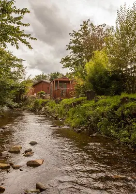 a stream with a house in the background next to a river at Bear Lodge in Auchterarder