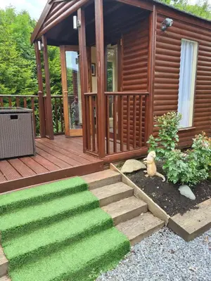 a wooden cabin with a green grassy path leading to a house at Bear Lodge in Auchterarder