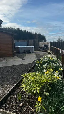 a garden with flowers and a bench on a patio at Lochinvar - Highland Log Cabin with Private Hot Tub in Airdrie