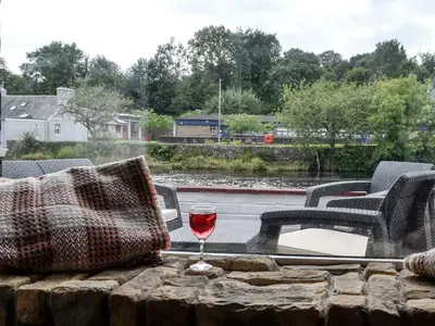 a glass of wine sitting on a table with chairs at Minnow Cottage in Newton Stewart