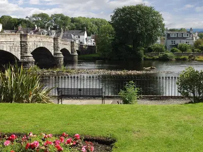 a bench next to a river with a bridge at Minnow Cottage in Newton Stewart