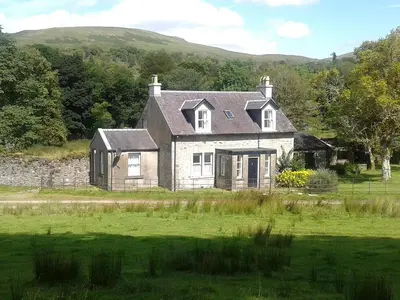 an old stone house in a field with a yard at Garden Cottage in Strachur