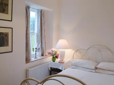 a white bedroom with a bed with a lamp and flowers at Garden Cottage in Strachur
