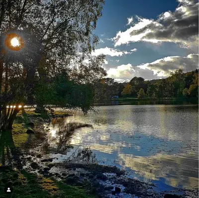 a view of a lake with the sun reflecting on the water at Loch Monzievaird Chalets in Crieff