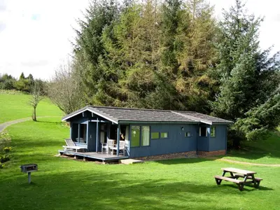 a blue cabin in a field with a picnic table at Loch Monzievaird Chalets in Crieff