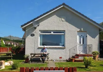 a man sitting on a bench in front of a house at Armadale Cottage in Lochgoilhead