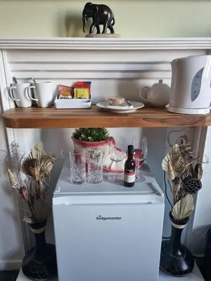 a shelf above a refrigerator with dishes and a bottle of wine at Knap Guest House in Tarbert