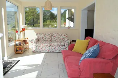 a living room with a red couch and a chair at Gorsnavoon Cottage in Clachaig
