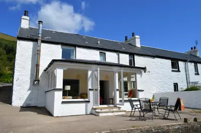 a white house with chairs and tables in front of it at Gorsnavoon Cottage in Clachaig