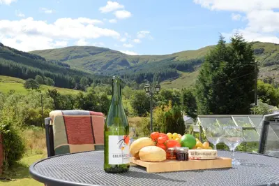 a table with a bottle of wine and a plate of fruit at Gorsnavoon Cottage in Clachaig