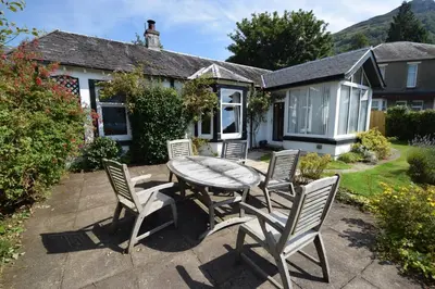 a patio with a table and chairs in front of a house at Ashburn Cottage in Lochgoilhead