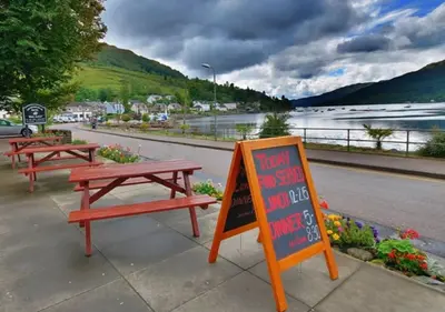 two picnic tables and a sign on the side of a road at Ashburn Cottage in Lochgoilhead