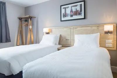 two beds in a hotel room with white sheets at The Raven’s Cliff Lodge by Marston's Inns in Motherwell