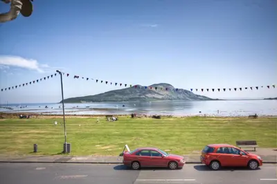 two cars parked on a street next to a beach at Lamlash Bay Hotel in Lamlash