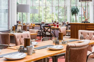 a restaurant with wooden tables and chairs and windows at Auchrannie Resort in Brodick