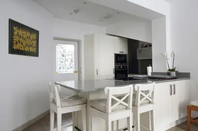 a kitchen with white cabinets and a counter with white stools at Quiet Ground Floor Mews Flat and parking in Edinburgh