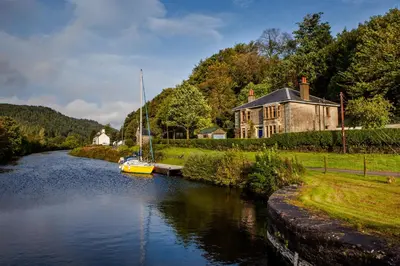 a boat is docked on a river next to a house at Shelburne Lodge in Cairnbaan