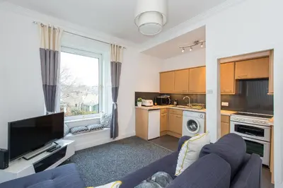 a living room with a blue couch and a kitchen at The Roseburn Apartment in Edinburgh