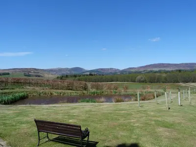 a park bench sitting in a field with a pond at Tulchan Lodge in Buchanty