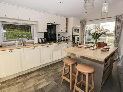 a kitchen with white cabinets and a counter and stools at Woodstock Lodge in Skelmorlie