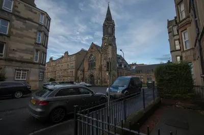 a car parked in front of a church with a clock tower at Stylish City Apartment - Near Haymarket, Walk to Castle and Princes Street in Edinburgh