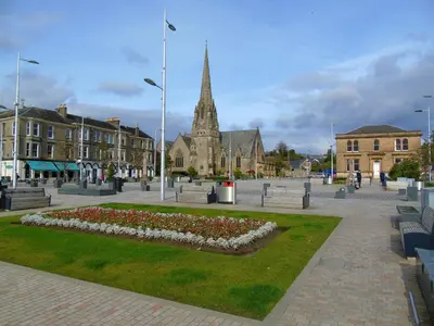 a town square with a park with flowers and a church at Snug - Meadhan Apartment in Helensburgh