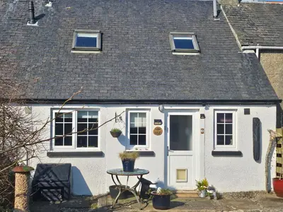 a white cottage with a white door and a table at 3 Knocknaha Cottage in Campbeltown
