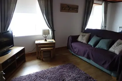 a living room with a purple couch and a tv at 3 Knocknaha Cottage in Campbeltown