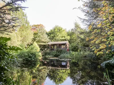 a garden with a house in the middle of a pond at The Log Cabin in Kilmore