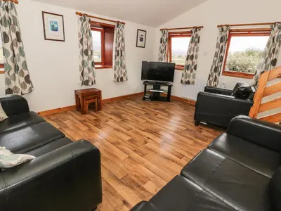 a living room with black leather furniture and wooden floors at The Byre in Newton Stewart
