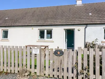 a house behind a fence with a clock on it at Starfish Cottage in Craignure