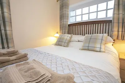 a bedroom with a large white bed with a window at Craigievern Cottage in Drymen