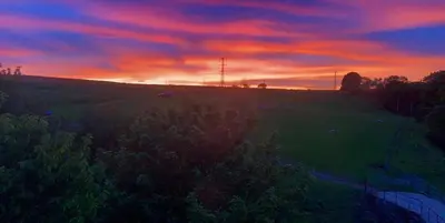 a sunset over a grassy field with a tree at Craigievern Cottage in Drymen