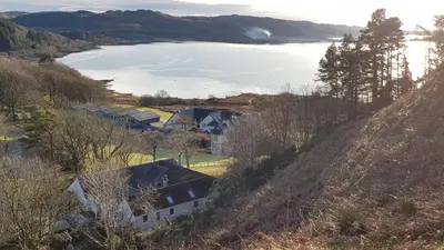 a group of houses on a hill next to a lake at The Old Cottage in Arduaine