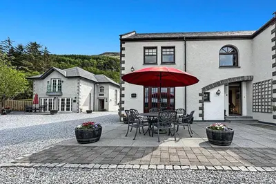 a table and chairs with a red umbrella in front of a house at Skyfall Glencoe at Creag ant Sionnaich Glencoe Ballachulish Highlands Near Fortwilliam in Glencoe