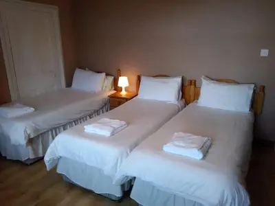 three beds in a room with a lamp on a table at Arbour Guest House in Oban