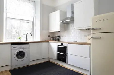 a kitchen with white cabinets and a washer and dryer at Stylish City Centre Apartments - D Terrace Residence in Edinburgh