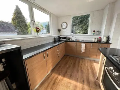 a large kitchen with wooden cabinets and two windows at A Spacious Flat with Character - Private Car Space in Paisley