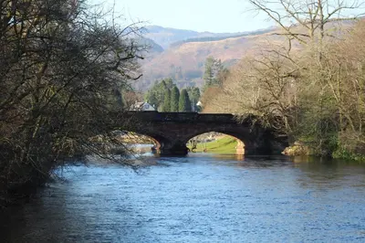 a bridge over a river with trees and mountains at Riverbank in Callander