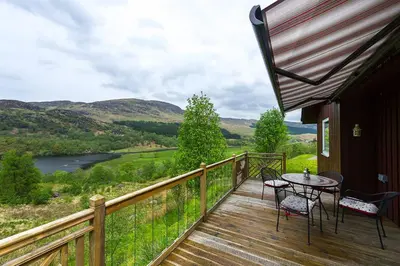 a balcony with a table and chairs and a view of a river at Kingfisher Lodge with sensational loch views in Crianlarich