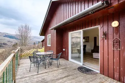 a patio with a table and chairs on a deck at Kingfisher Lodge with sensational loch views in Crianlarich