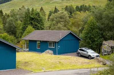 a blue house with a car parked in front of it at 2 bedroom lodge with stunning loch mountain views in Crianlarich