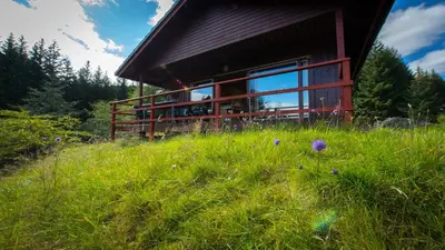 a building in a field of grass with flowers in front of it at 2 bedroom lodge with stunning loch mountain views in Crianlarich