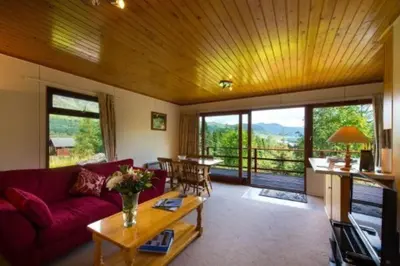 a living room with a red couch and a table at 2 bedroom lodge with stunning loch mountain views in Crianlarich